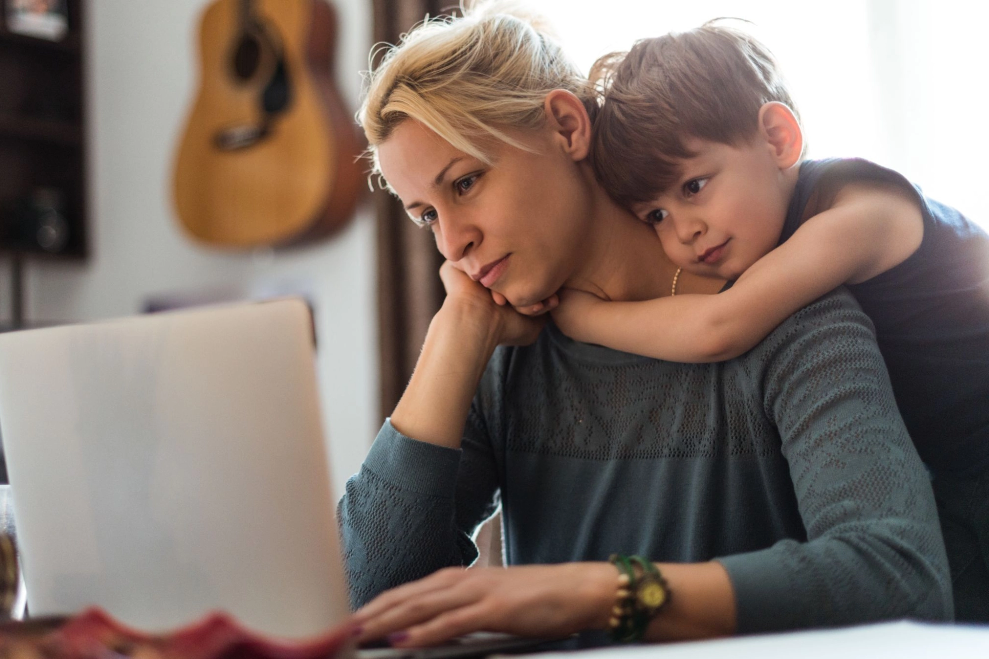 Mutter sitzt am Laptop, während ihr Sohn sie umarmt