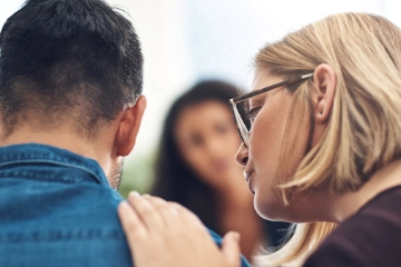 Eine Frau spricht mit einem Mann und legt ihm dabei die Hand auf die Schulter.